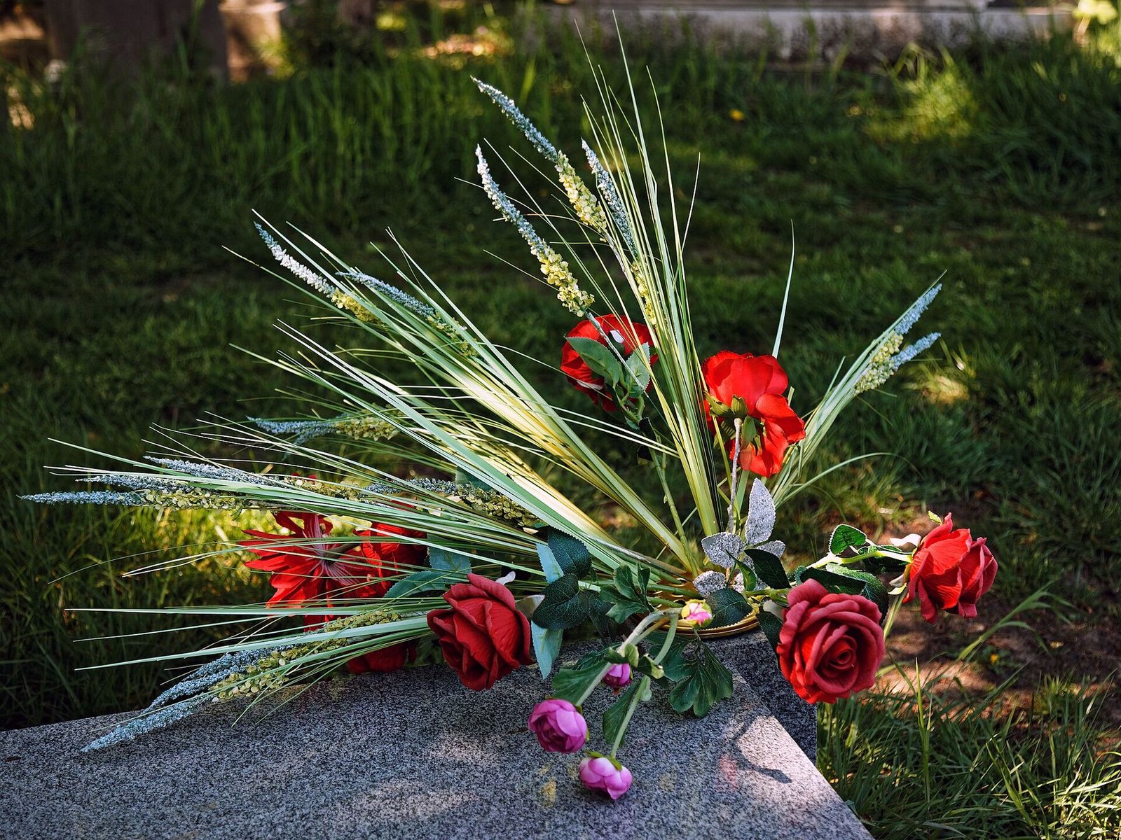 A well-kept grave with a rose and heather floral arrangement resting on a clean headstone